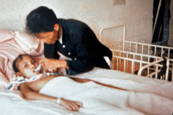 Sick child being fed in a bed by a nurse during the Vietnam war