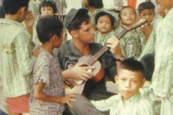 America GI playing guitar and children